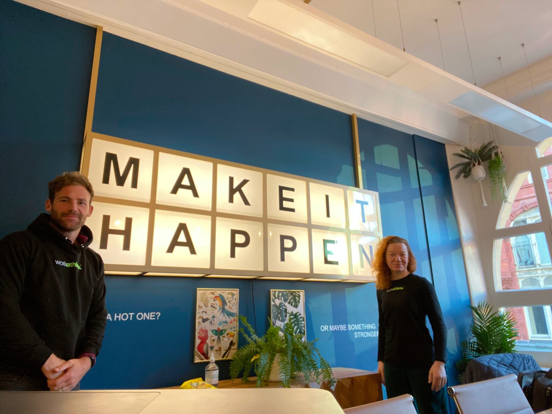 Workathelete coaches and speakers standing next to make it happen signage hung on the wall